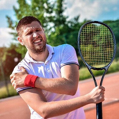 male tennis player holding shoulder and grimacing 