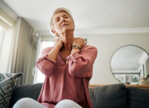 Senior woman sitting on sofa, dealing with neck pain 