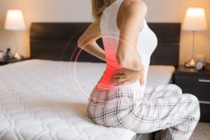 Woman sitting on her bed, suffering from lower back pain 