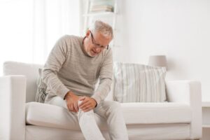 Senior man sitting on sofa, suffering from knee pain 